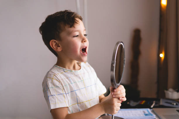 istock Cute little boy pronouncing sound O looking at mirror doing an online Speech therapy lesson through a laptop 1409489638