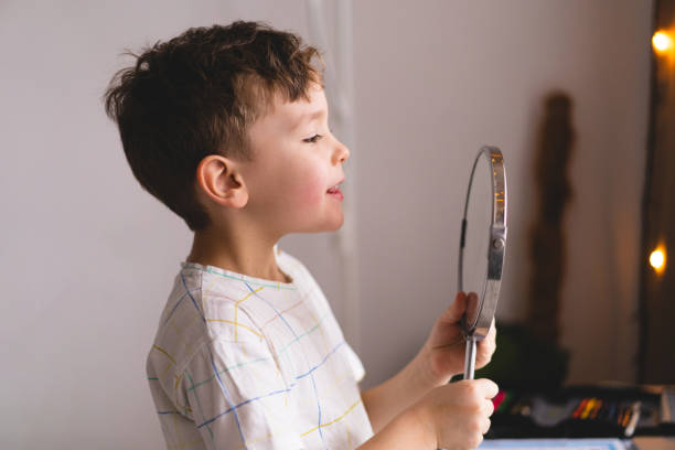 istock Cute little boy pronouncing sound O looking at mirror doing an online Speech therapy lesson through a laptop 1409489660
