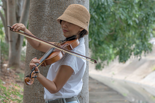 Beautiful asian woman hold violin on nature background, in emotion happy feeling.