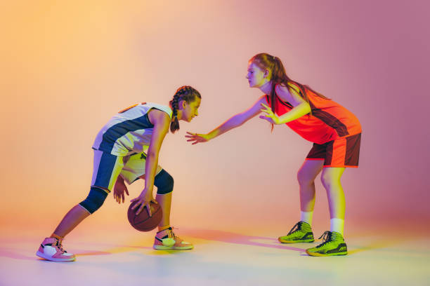 attaque et défense. joueuses de basket-ball, jeunes filles, adolescentes en action avec ballon isolé sur fond néon. concept de sport, équipe, enegry, compétition, compétences - child basketball uniform sports uniform photos et images de collection