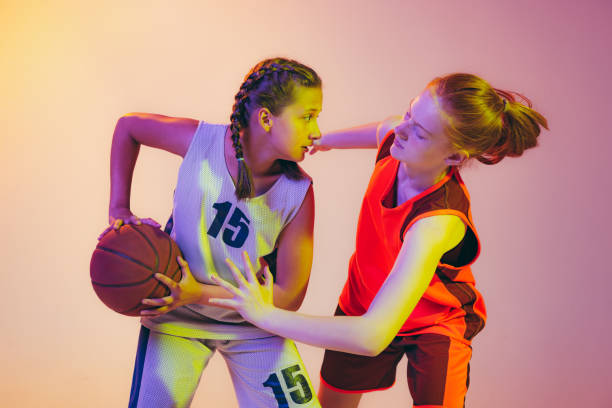 攻撃と防御。女性バスケットボール選手、若い女の子、ネオンドの背景に隔離されたバスケットボールボールで行動中の十代の若者。スポーツ、チーム、エネグリー、競争、スキルの概念 - basketball team sports healthy lifestyle isolated objects ストックフォトと画像