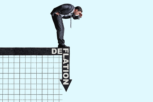 A man stands on top of an arrow that precipitously  drops to illustrate the concept of deflation.