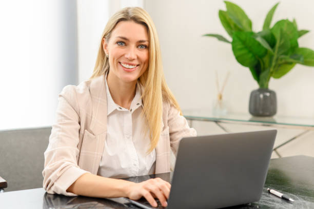 istock Smiling business woman using laptop for remote work from home. Confident lady checking emails, conducting business correspondence while sitting at the table 1409491350