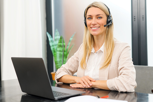 Young female call center operator with hands-free headset talking with client in home office. Concept of remote work. Waist up portrait view