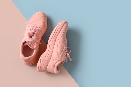 Pink female sneakers or sport shoes on blue and pink background. View from above. Flat lay. Concept sale and shopping.