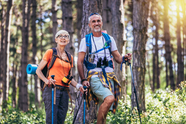 coppia di anziani che camminano nella foresta indossando zaini e bastoncini da trekking. - anziani attivi foto e immagini stock