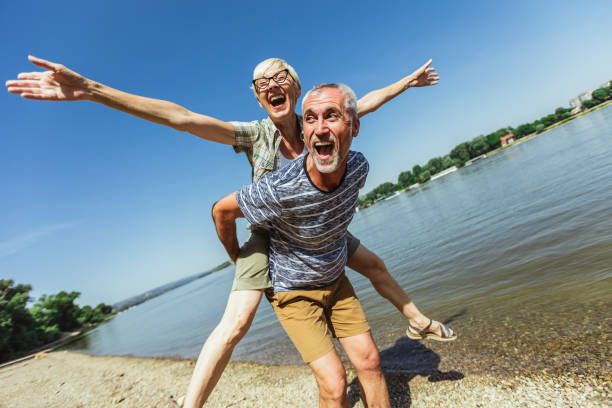 Portrait of happy mature man being embraced by his wife at the beach. stock photo