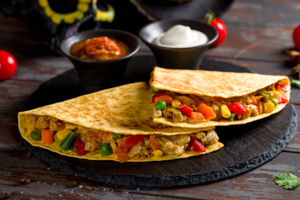 istock Mexican Quesadilla with chicken, vegetables, cheese and sauces on black stone plate 1409496468