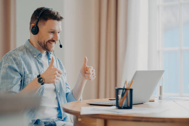istock Satisfied bearded male model attends online training from home uses headset makes like gesture with both hands looks attentively at laptop computer makes video call poses against cozy interior 1409497798