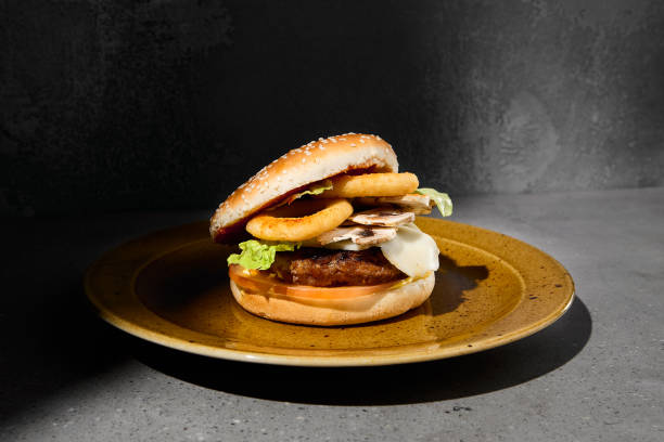 istock American burger with onion rings on ceramic plate in dark minimal style. Beef burger on gray stone table with hard shadow. Fast food dark concept. Burger on gray concrete background. Simple food menu. 1409501418