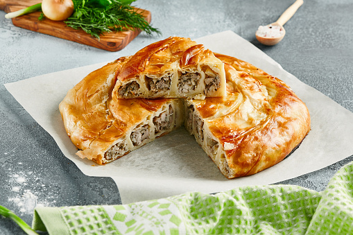 Classic turkish pie with meat on wooden board. Composition with burek pie on concrete background with textile and spices. Balkan pie with minced meat  in rustic style on gray table