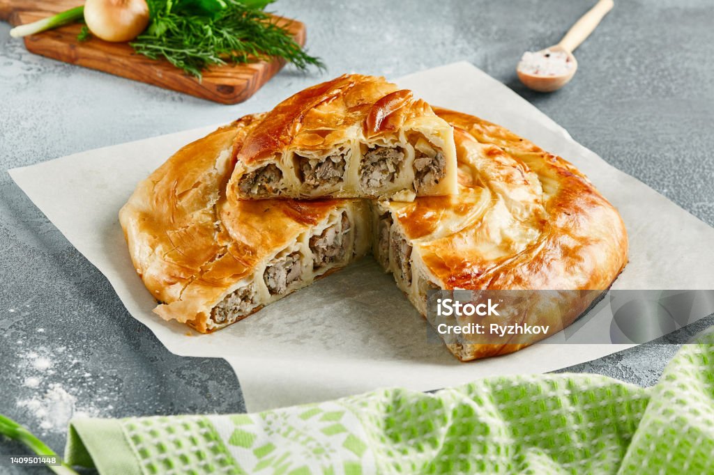 Classic turkish pie with meat on wooden board. Composition with burek pie on concrete background with textile and spices. Balkan pie with minced meat  in rustic style on gray table. Classic turkish pie with meat on wooden board. Composition with burek pie on concrete background with textile and spices. Balkan pie with minced meat  in rustic style on gray table Pita Bread Stock Photo