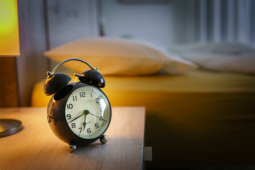 Close up of a black alarm clock at 6:43am on the night table with bed at background. Selective focus on alarm clock. High resolution 42Mp indoors digital capture taken with SONY A7rII and Zeiss Batis 40mm F2.0 CF lens