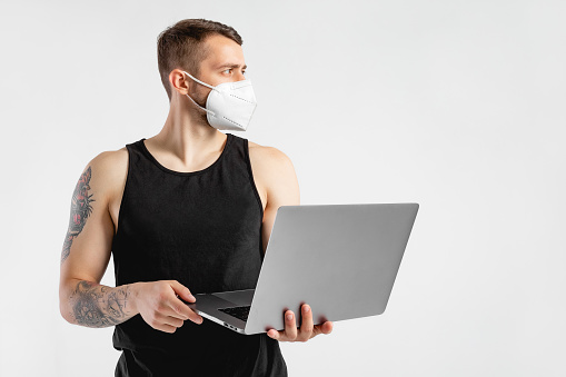Male portrait of sports man in studio. Caucasian men on background. Fitness concept for exercise and muscular build. Professional athlete, fit photography. Person with coronavirus face mask and laptop