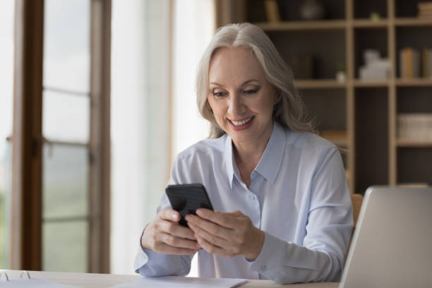 istock Smiling middle-aged businesswoman using smartphone seated at workplace 1409509173