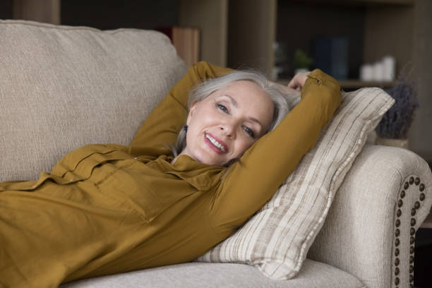 istock Beautiful aged woman lying on couch smiling look at camera 1409509272