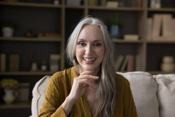 istock Beautiful older woman sit on sofa smile look at camera 1409509292
