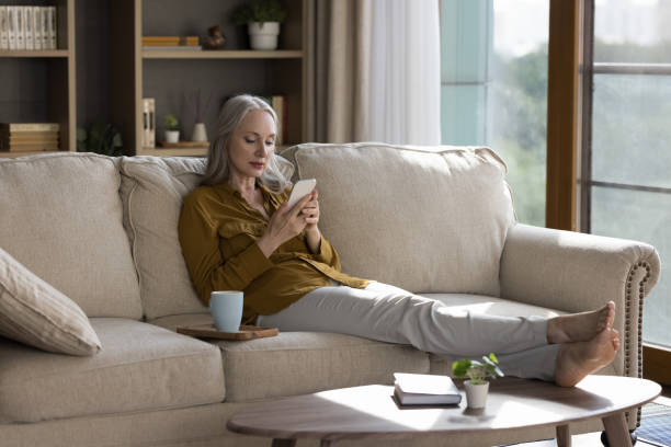 istock Middle-aged woman relaxing on sofa with modern smartphone 1409509315