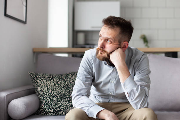 istock Thoughtful bearded man sitting on sofa at home. Handsome man looking away thinking about solving problems. 1409511546