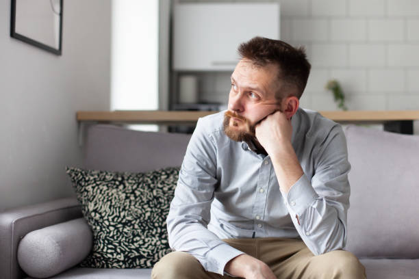 Thoughtful bearded man sitting on sofa at home. Handsome man looking away thinking about solving problems. stock photo