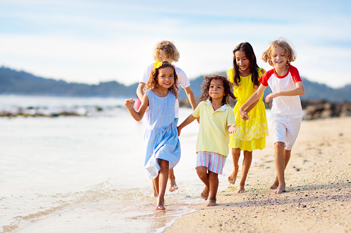 Group of kids playing on tropical beach. Children play at sea shore. Water and sand fun. Summer vacation. Travel with kids. Ocean holiday with child. Boy and girl run and jump.