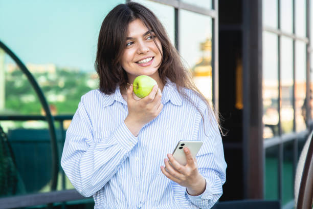 istock A young woman eats an apple with a smartphone in her hands. 1409512298
