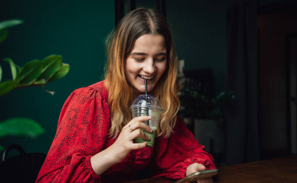 young woman drinking green drink ice matcha latte in cafe and using smartphone. - blueberry smoothie milk shake drink imagens e fotografias de stock