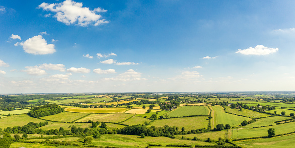 A panoramic aerial image over a rolling landscape of fields separated by traditional hedgerows and small woodland, in the English Midlands.