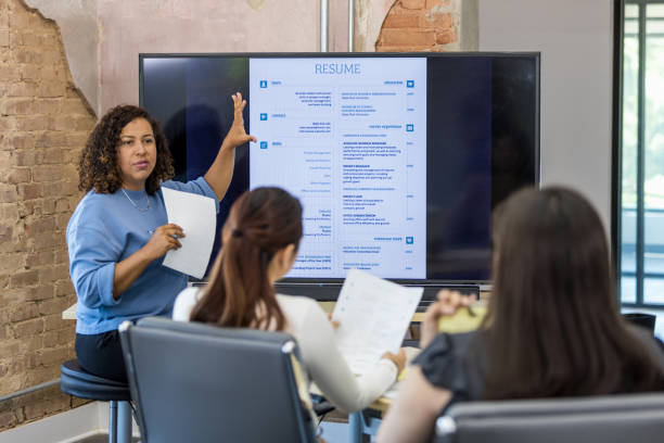 Mid adult human resources representative leads a resume building class A female mid adult human resources representative leads a resume building class. She uses a large projection screen. good cv stock pictures, royalty-free photos & images