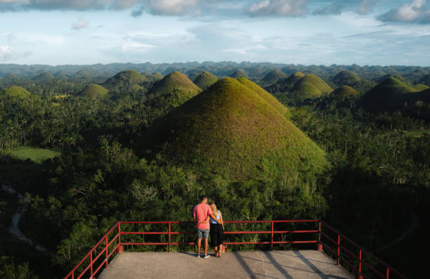A young couple of travelers enjoy panoramic views at sunset in the Chocolate Hills of Bohol, Philippines Incredible views of the chocolate hills mountains in bohol, philippines chocolate hills photos stock pictures, royalty-free photos & images
