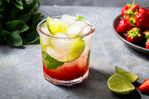 cold detox water with lime, strawberry, mint in the glass with ice cubes on gray background