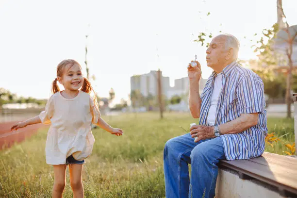 Photo of Grandfather blowing soap bubbles to his grandchild