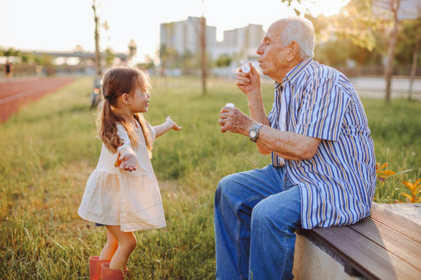 abuelo soplando pompas de jabón a su nieto - bubble child bubble wand blowing fotografías e imágenes de stock