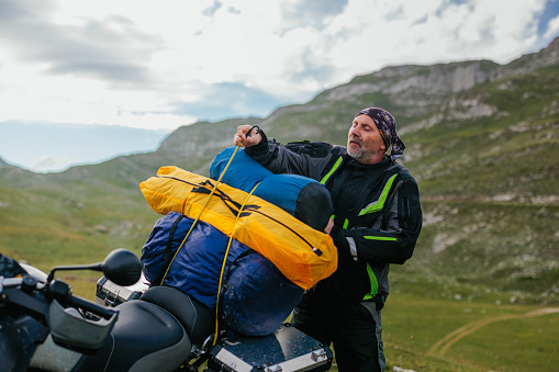 Mature traveler on a motorcycle unpacking his luggage somewhere in the mountain