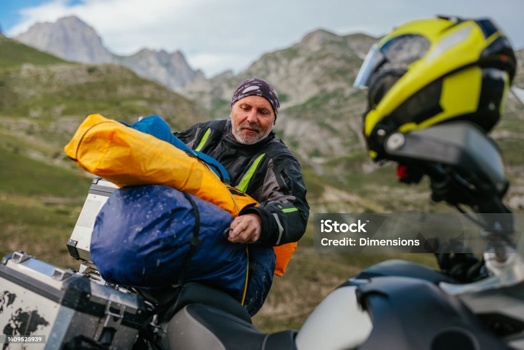 Packing stuff. It's time for continuing ride after night spent in mountains A biker is packing his camping gear onto his bike as he prepares to continue his journey in the mountains Motorcycle Stock Photo