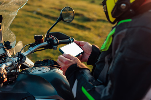 Close up of biker's hands holding a phone with a blank screen. The biker is sitting on his motorbike