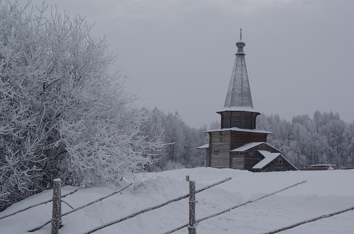 wooden church of the Russian Orthodox Church covered with snow in the outback of the Vologda region in winter against the backdrop of a forest in cloudy weather