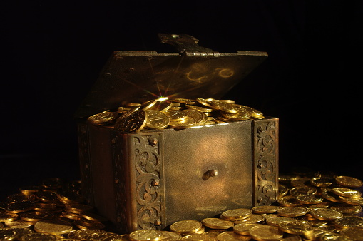 close-up shot of an iron chest with coins and standing on coins on a black background