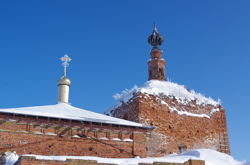 Towers of an old Russian Orthodox church made of red brick with domes and crosses in winter against a blue sky