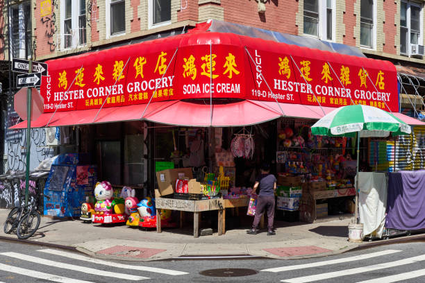 New York, NY - June 29, 2022: A corner grocery store in Chinatown, NYC with a shiny bright red awning. Many items for sale are on display on the sidewalk.