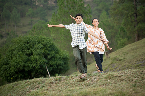 Teenage brother and sister having fun with arms outstretched on grass hill