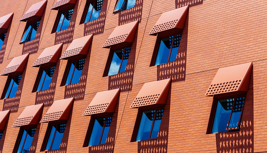 Modern orange brick wall, windows with with blue sky-reflections, awnings, and shadows.