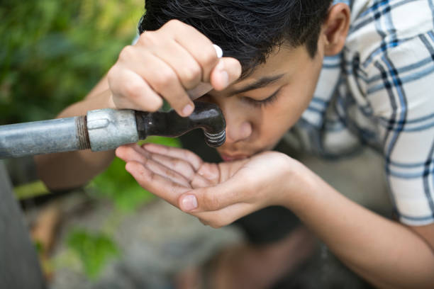Thirsty teenage boy drinking tap water outdoors in field