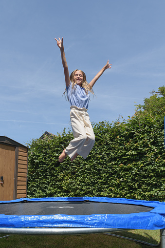 Happy teenage girl jumping on trampoline outdoors.