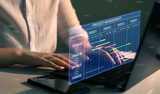 Business Project Management System. Project manager working on laptop and updating tasks and milestones progress planning with Gantt chart scheduling interface for company on virtual screen