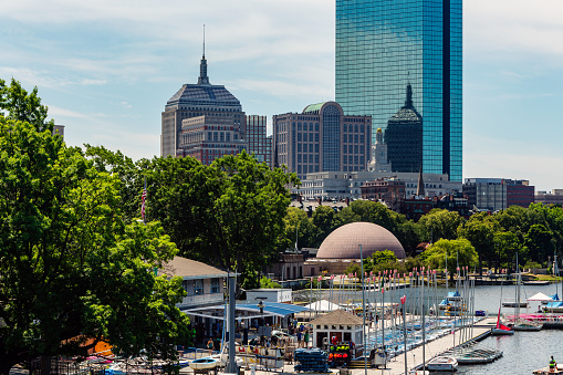 Boston, Massachusetts, USA - July 15, 2022: View of the Community Boating organization sailing marina on the Charles River Esplanade between the Hatch Shell and the Longfellow Bridge. The Back Bay skyline, including the John Hancock Tower, is in the background.
