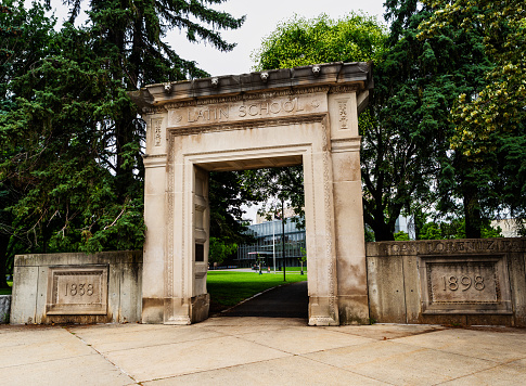 Cambridge, Massachusetts, USA - July 16, 2022: The old Cambridge High and Latin building was demolished in 1980, but the old granite lintel and doorway frame have been put in place at the corner of Ellery Street and Broadway as a commemorative archway, leading into the grassy fields of Joan Lorentz Park, which is immediately in front of the Cambridge Public Library. The library building is visible through the arch.