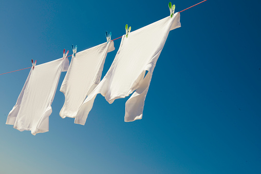 Clean child's clothes hanging on laundry line against light blue background