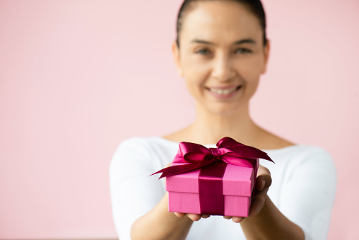 Smiling woman holding pink gift box infront of pink background.