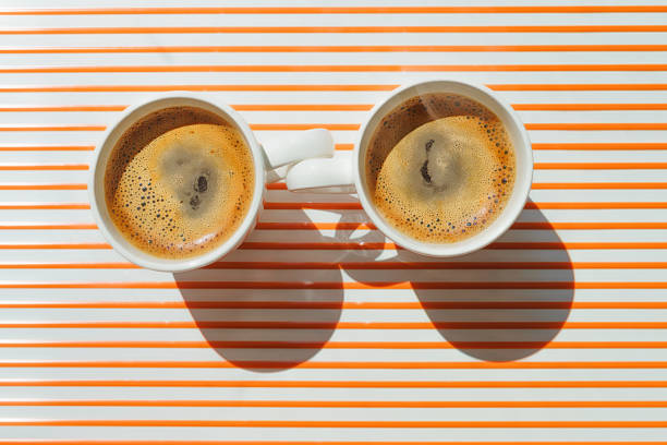 istock Two white coffee cup close one to other on orange striped table top view 1409537775